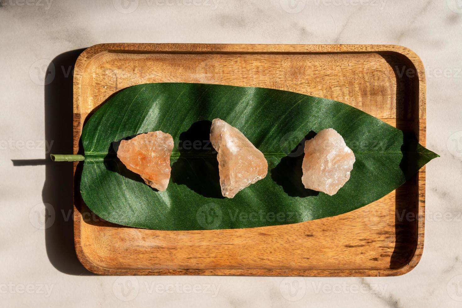 Top view of crystals of pink himaayan salt on green leaf background. Stone therapy and massaging concept. photo