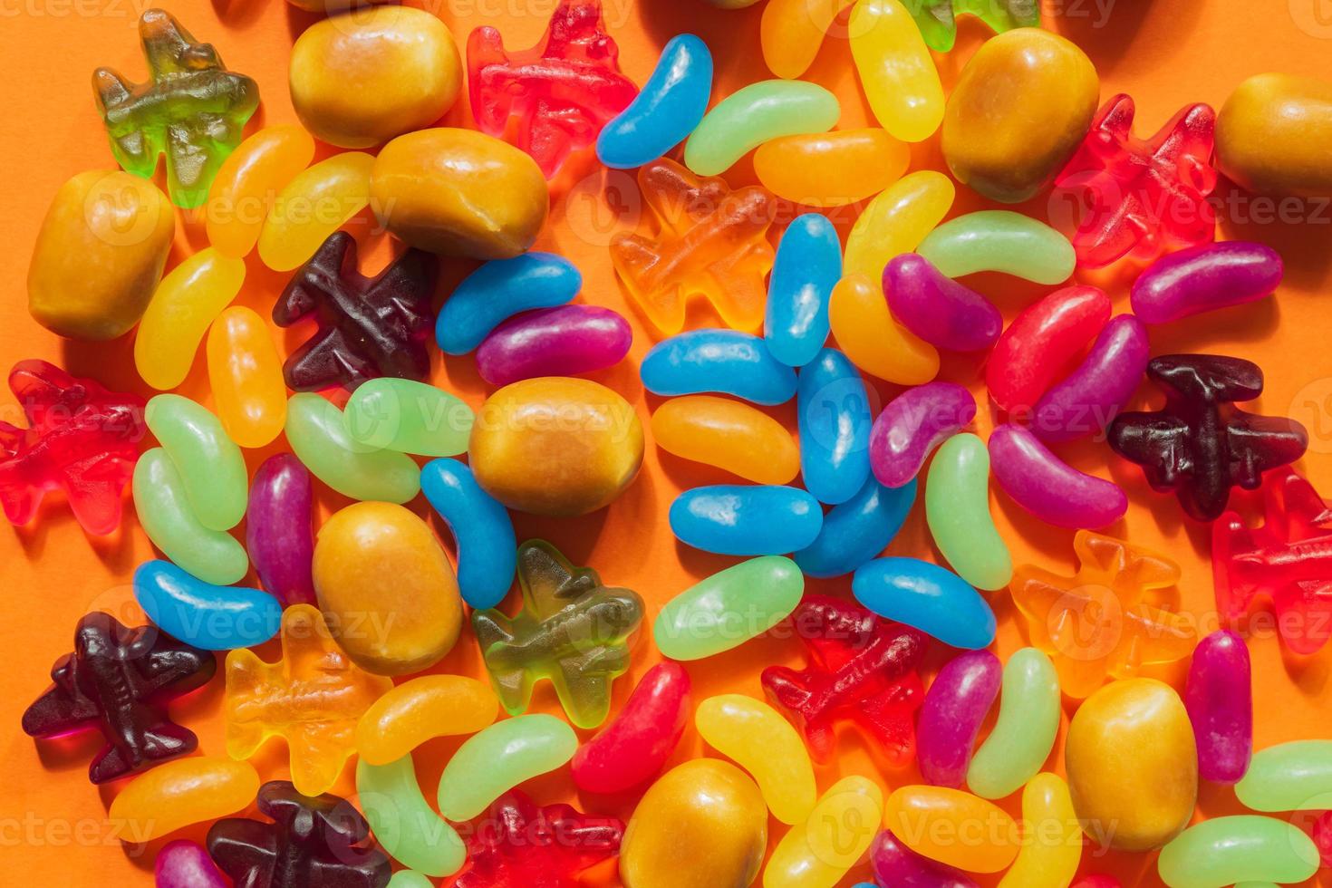 Multi-colored glazed jelly beans sweets on orange paper background photo