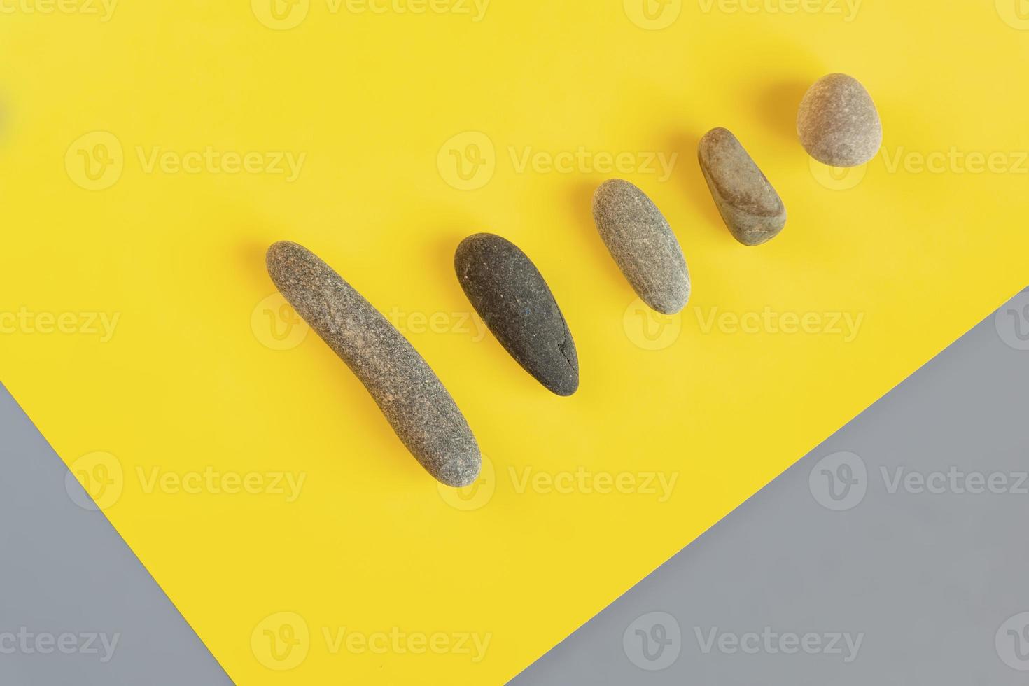 Flat lay in a trendy 2021 new colors. Illuminating Yellow and Ultimate Gray. Color of the Year 2021. Grey sea stones on yellow background. photo