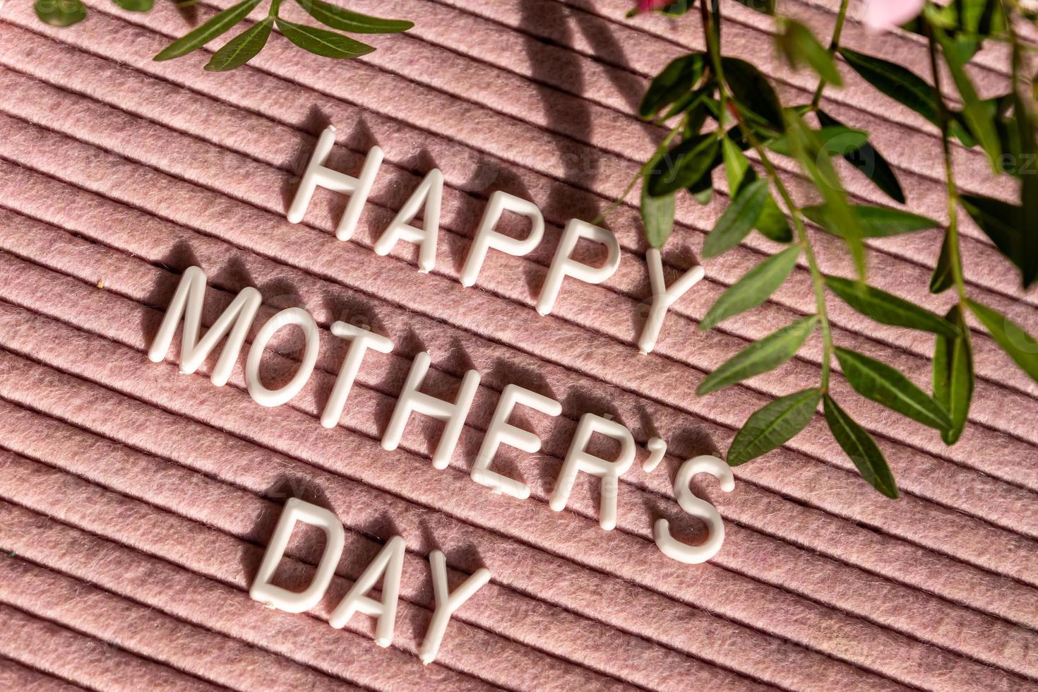 Pink letterboard with quote Happy Mother's Day, decorated with green leaves on pink background. Festive greeting card photo