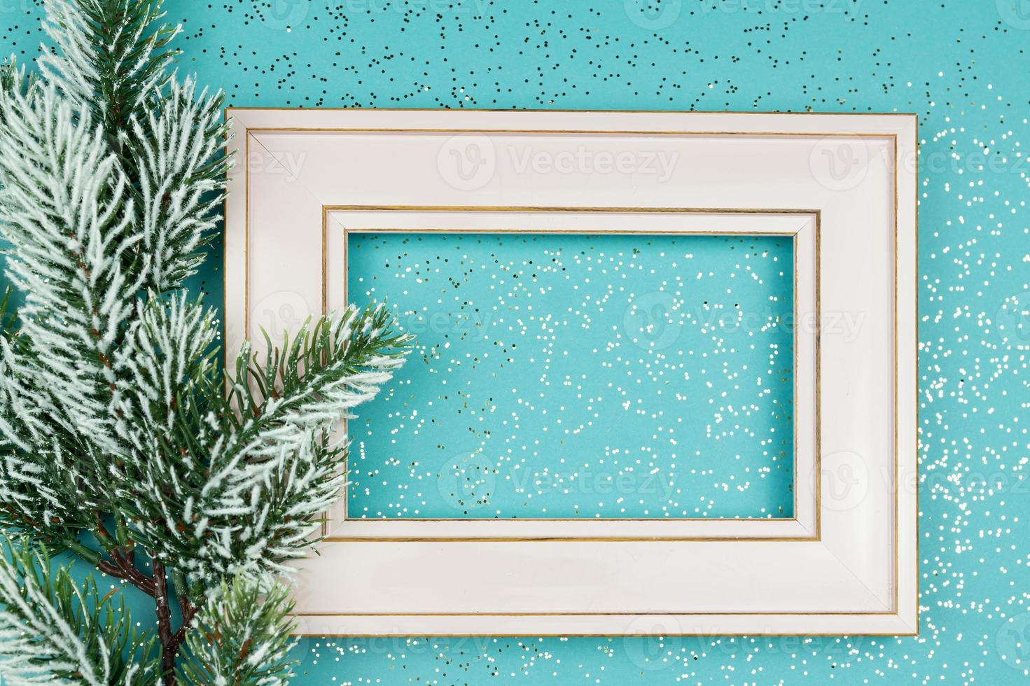 Festive greeting card for Christmas with photo frame, spruce tree branch on blue confetti background.