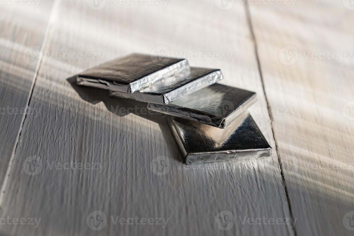 Mini chocolate bars in silver paper on white wooden background. Natural cocoa product in portion package. photo