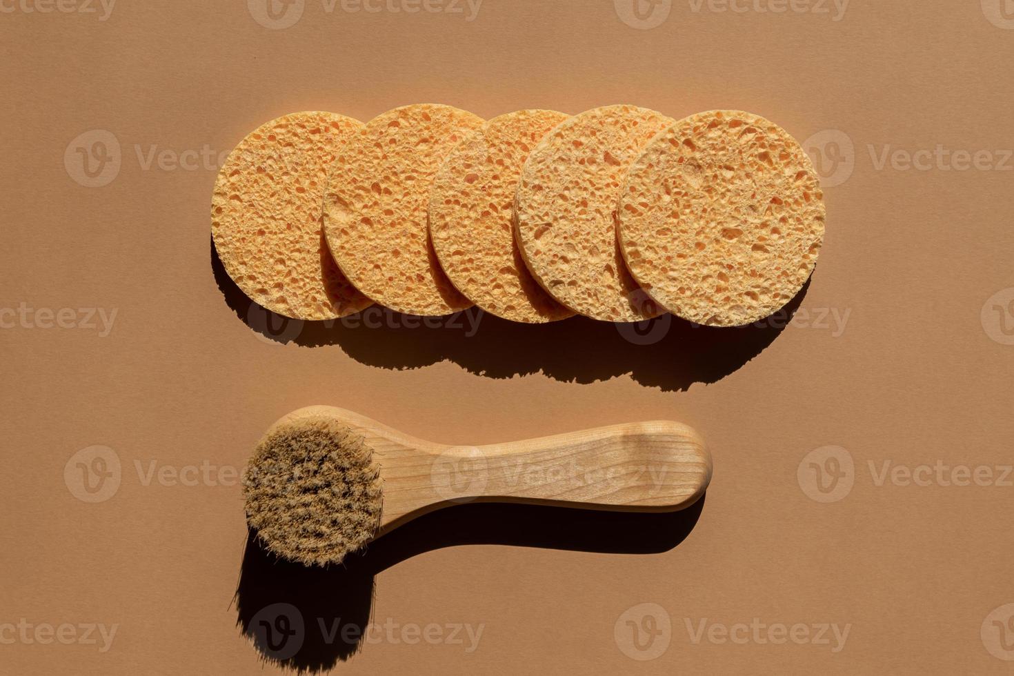 Shower accessories - face brush with natural bristle and round cellulose sponges on a brown background, top view. Cleansing of the skin health concept. Flat lay photo