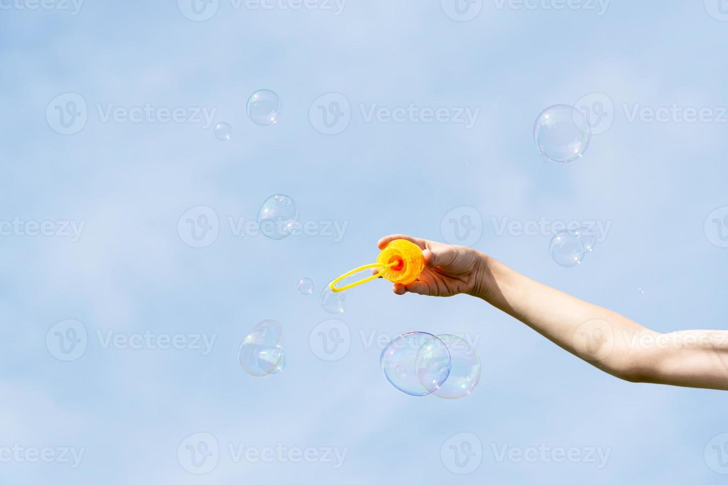 childs hand holding a wand for blowing soap bubbles against the blue sky on a sunny summer day. photo