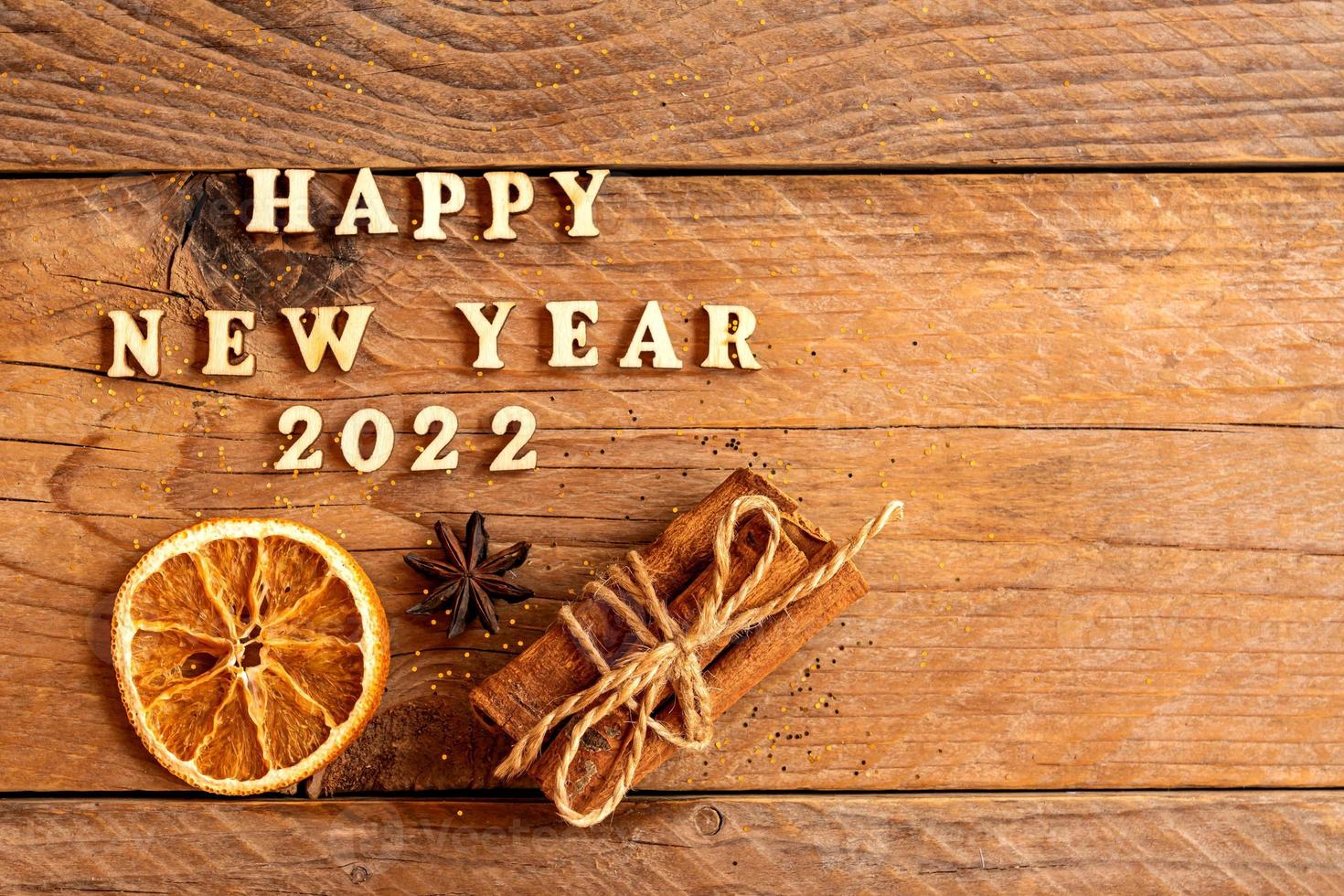 Cinnamon sticks, slices of dried orange, star anise and quote happy new year 2022 on wooden background with copy space. Top view. Christmas and New Year celebration concept. photo