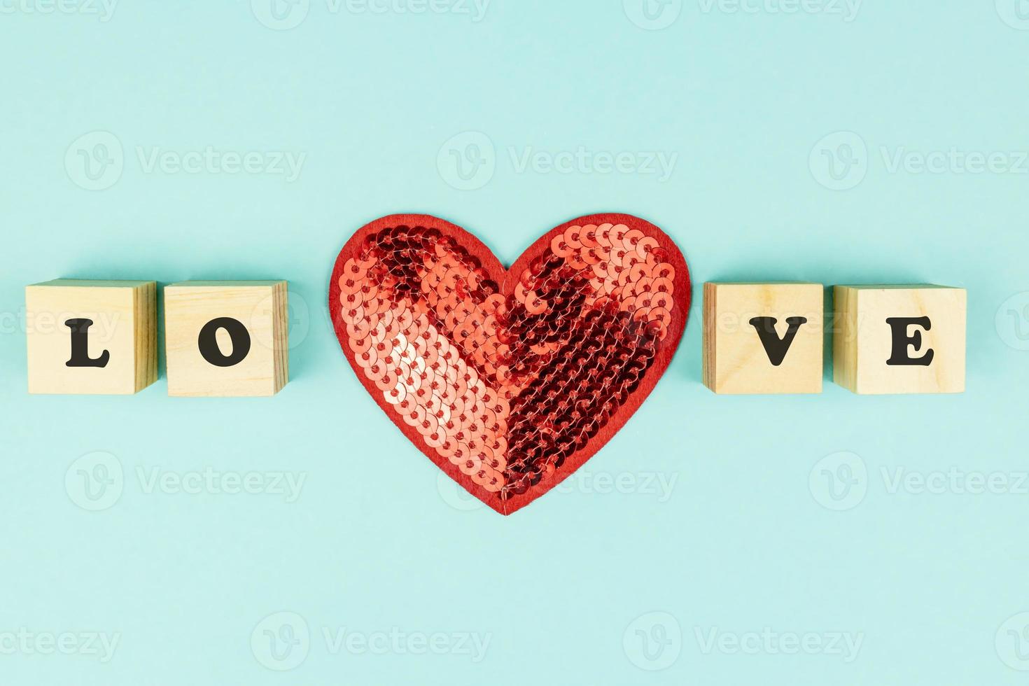 Creative flat lay in minimal style. Red sequins heartand wooden cubes with text LOVE on blue background. Festive greeting card with opy space. photo