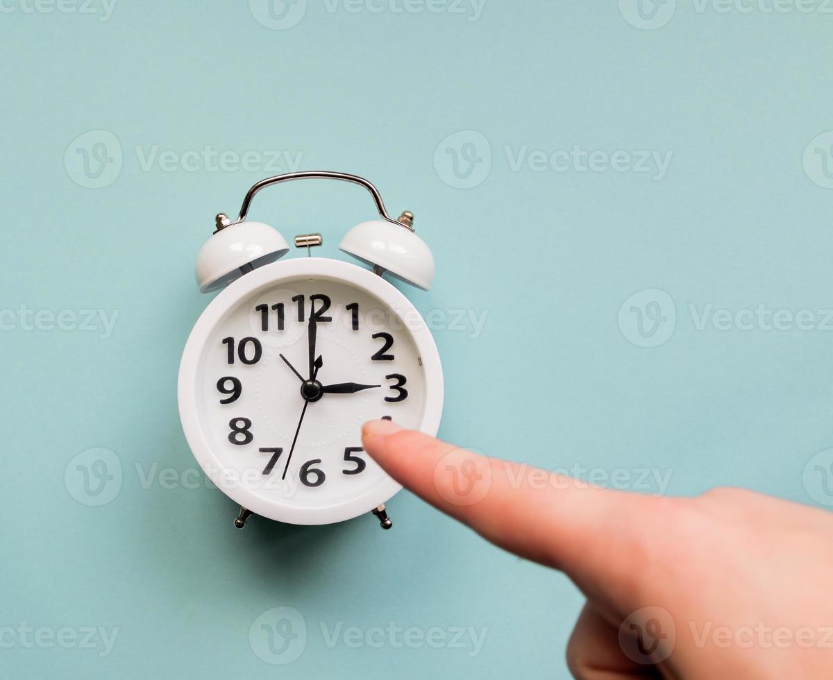 Female hand pointing on white alarm clock. Deadline and business concept photo