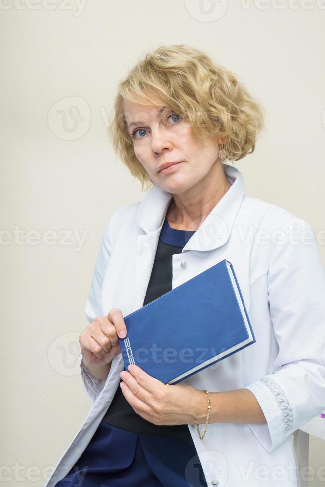 middle aged woman in white coat holding blue daily planner. Doctor female, medical professional photo