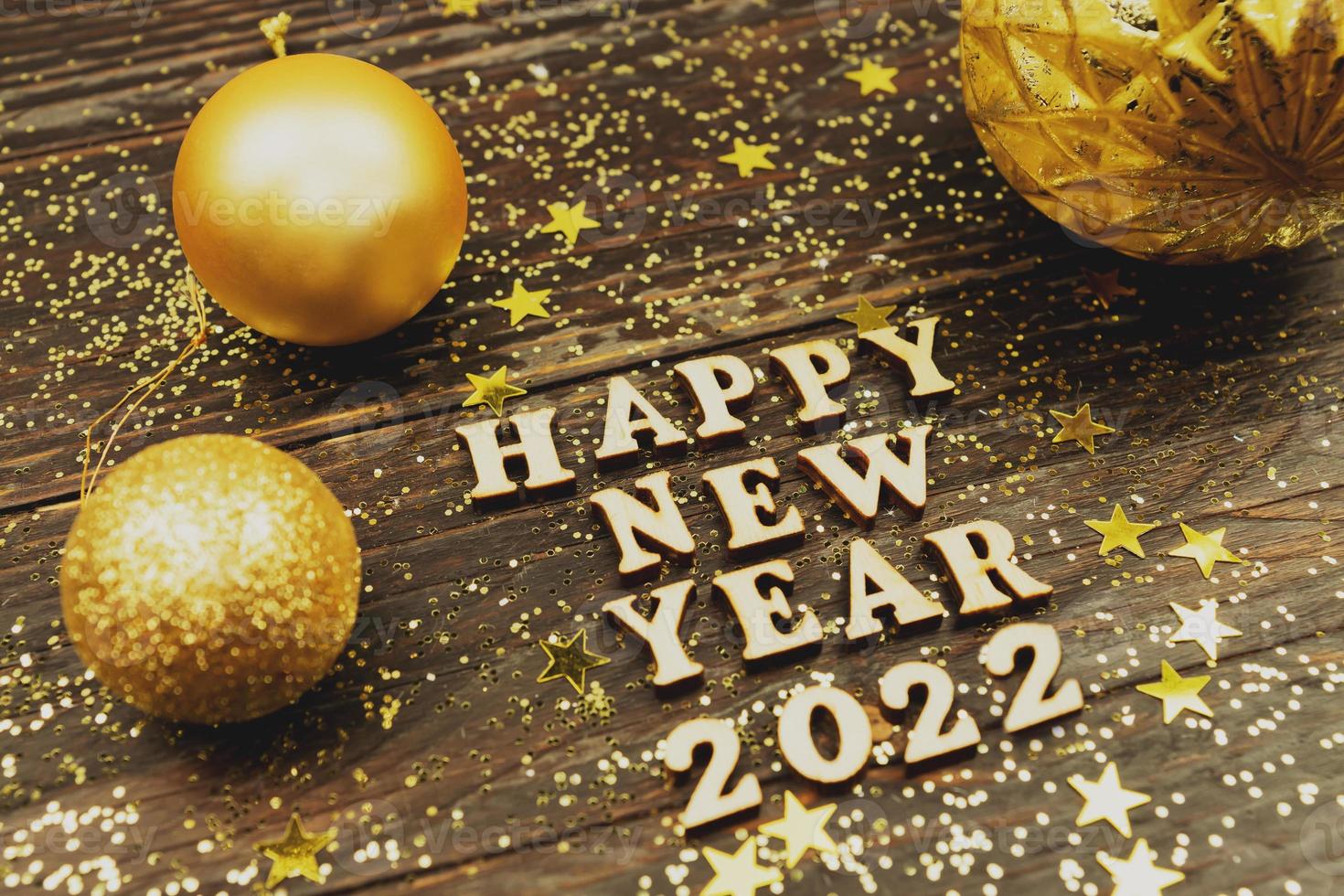 Happy new year 2022 text on wooden background surrounded golden christmas toys and fur tree branch. Festive greeting catd for holidays photo