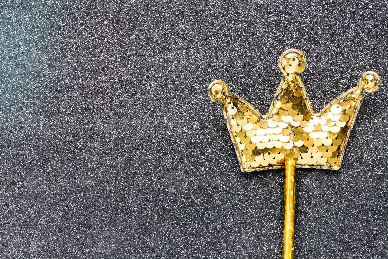 golden magic stick from sequins in crown shape on black glitter background. Creative flat lay close up photo