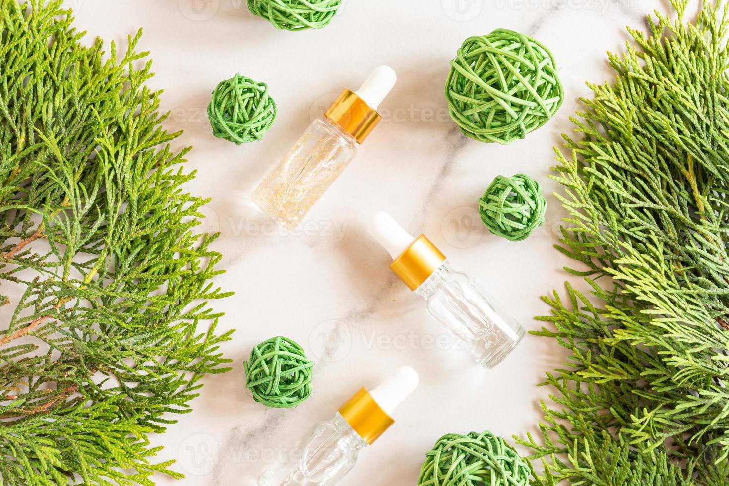 Glass dropper bottles with cosmetic oil, essential or serum on marble background with thuja branches and ratang balls. Concept of natural organic cosmetics. Herbal homeopathic products. photo