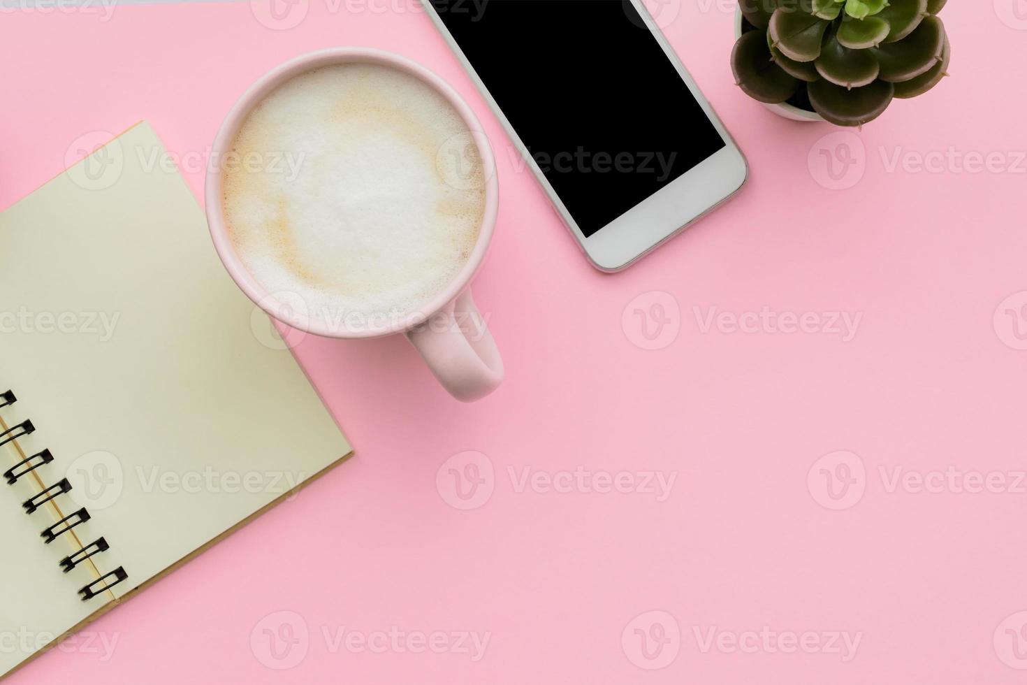 feminini desk workspace with smartphone, blank notepad, cactus, cup of coffee on pink background. flat lay, top view photo