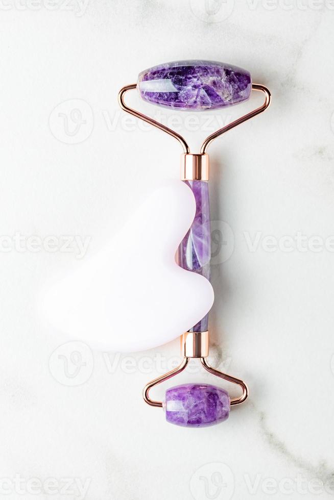 Face quartz roller, massager guasha scraper, made of natural quartz stone. Self-care set. homemade Spa products on a marble background, the concept of Spa and Wellness with space for text photo