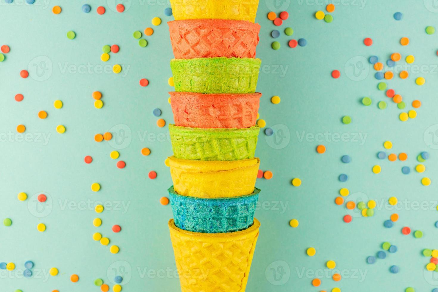 bright multicolored ice-cream waffle cones on blue background with scattered confetti sugar sprinkles. photo