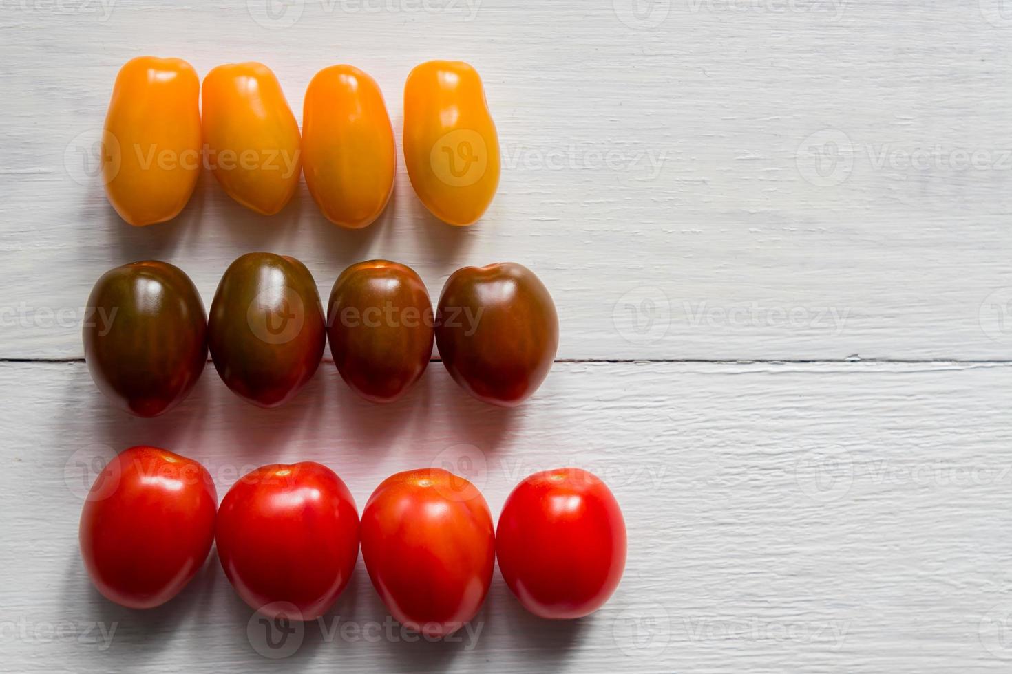 Three rows of different sorts of cherry tomatoes. Yellow, red and green. Organic ripe tomato on wooden table, top view. photo