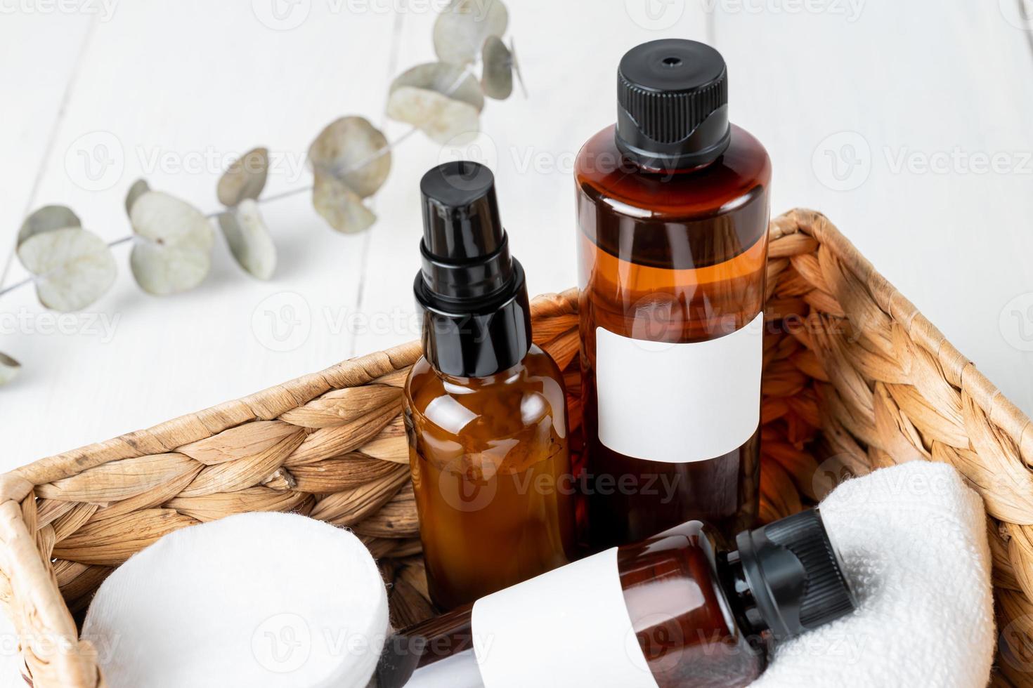 Facial and body care cosmetics dark glass bottles composition in eco basket with dry eucalyptus branch. Beauty face oil, spray toner, cream jar unbranded blank packages. Skincare female products photo