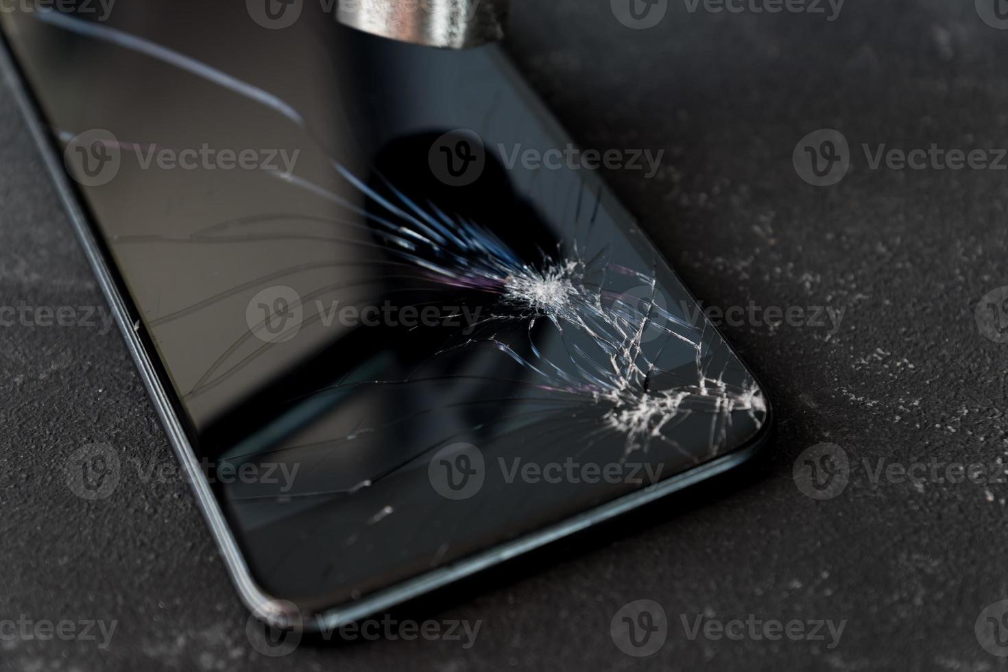 smartphone con pantalla de cristal rota y martillo sobre fondo oscuro. foto