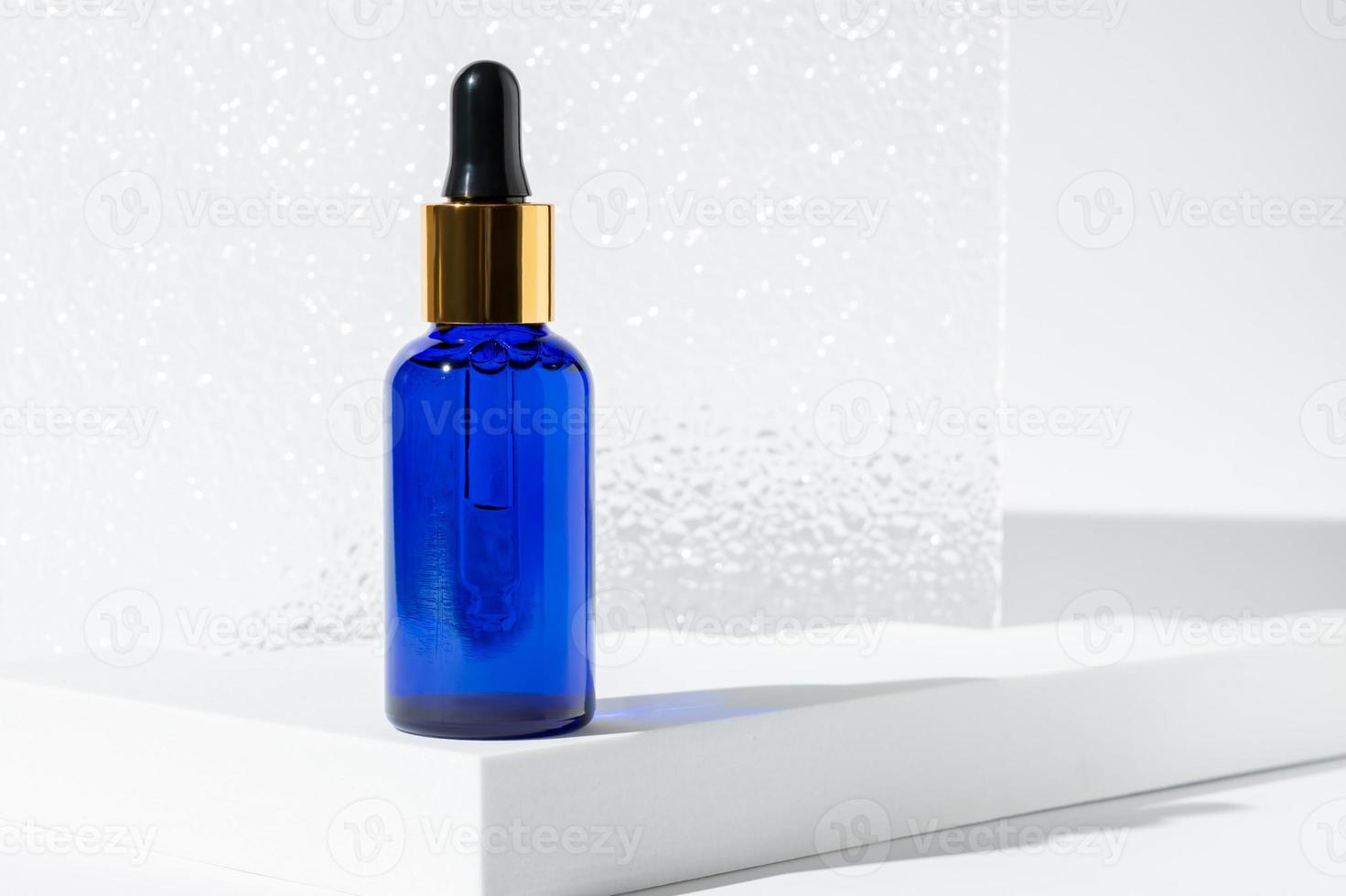 Glass cosmetic bottle with oil or serum for skin care on white podium with hard shadows. Natural skin care concept. Oily cosmetic pipette. Trendy shoot photo