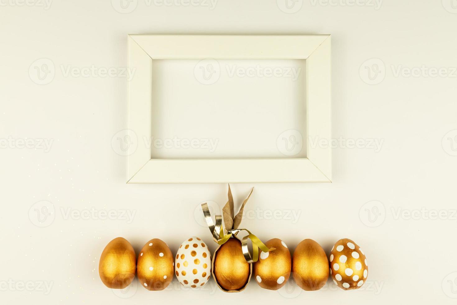Easter festive decoration. Top view of easter eggs colored with golden paint and empty mock-up photo frame. Various dotted designs. White background.
