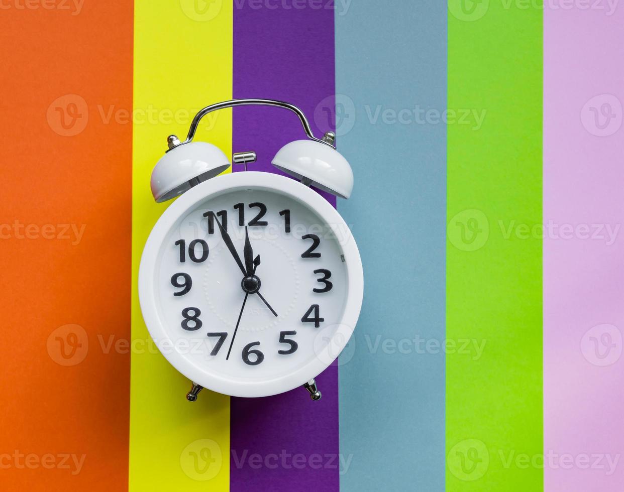 white alarm clock on multicolored striped background with copy space for text. photo