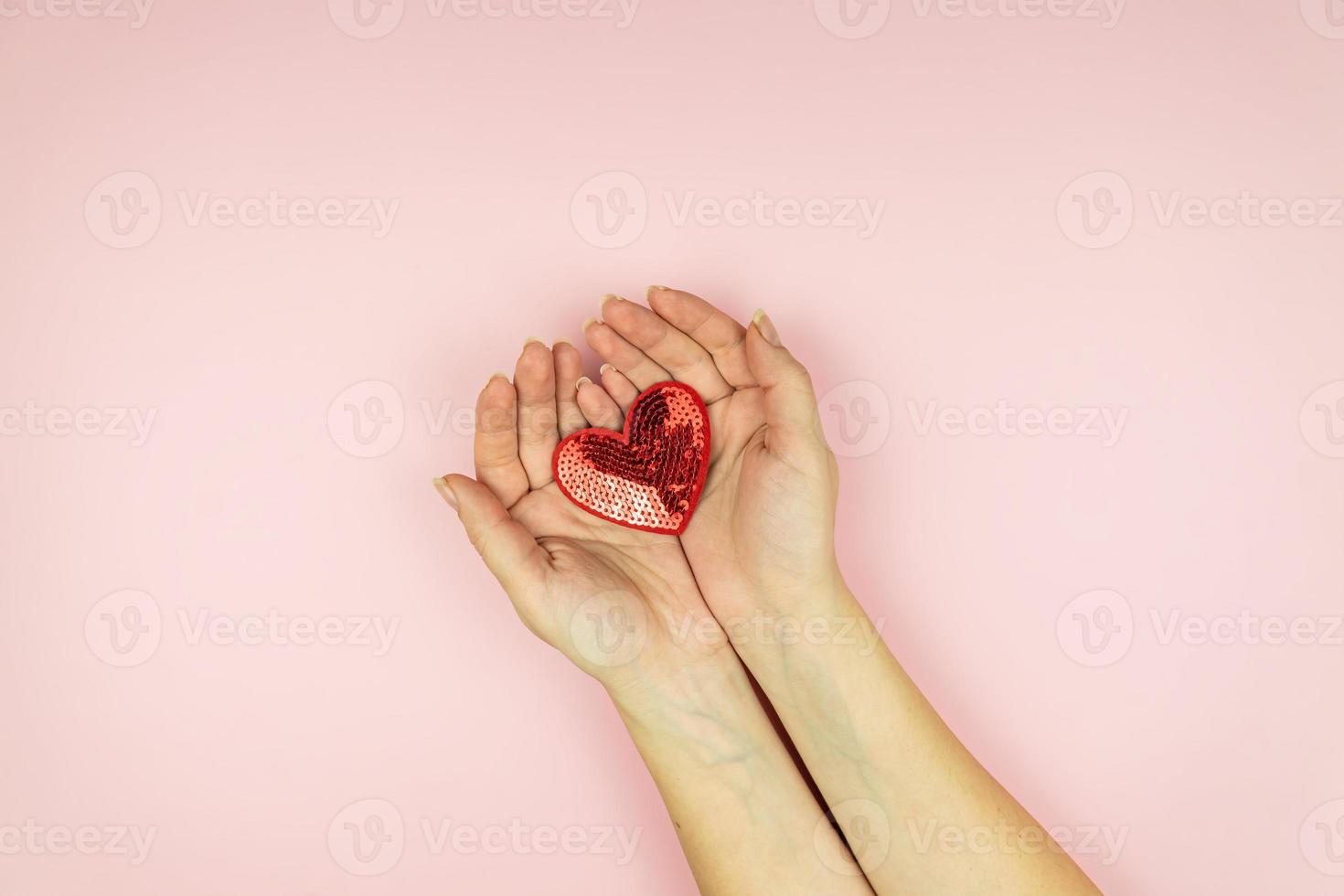 Female hands holding red sequin heart on pink background. Creative minimal layout with copy space photo