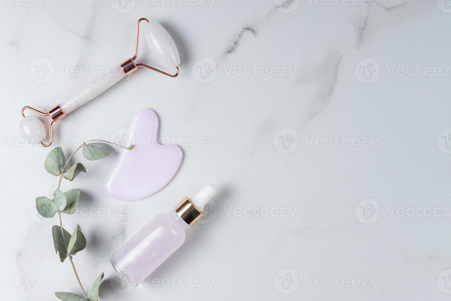 rodillo de masaje de cuarzo rosa y herramientas de raspado de piedra gua sha y eucalipto seco sobre fondo de mármol. plano, vista superior, belleza estética, cuidado de la piel, concepto de tratamiento de bienestar foto