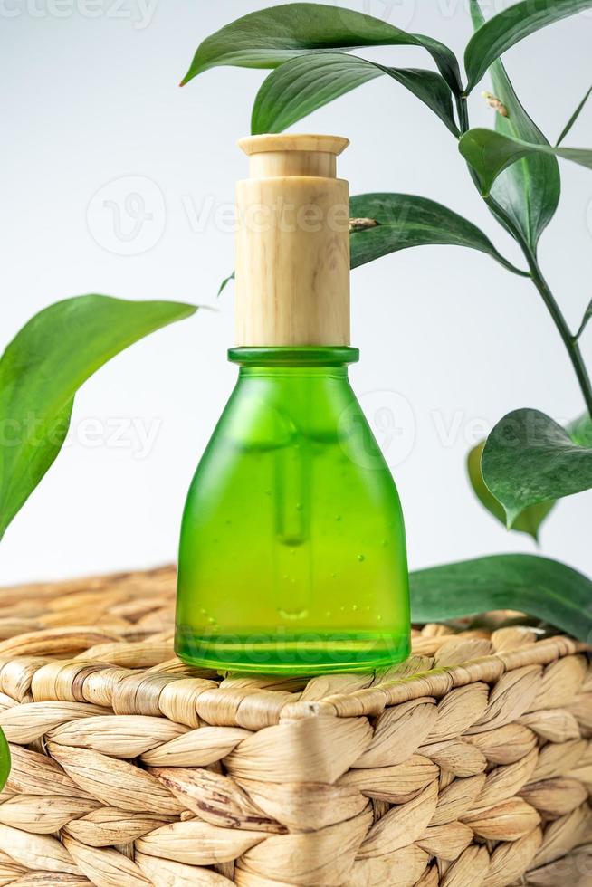 Green frosted cosmetic bottle with pipette on wooden podium, product packaging with natural ruscus branch, anti aging serum with peptides, cosmetics mockup, spa concept. photo