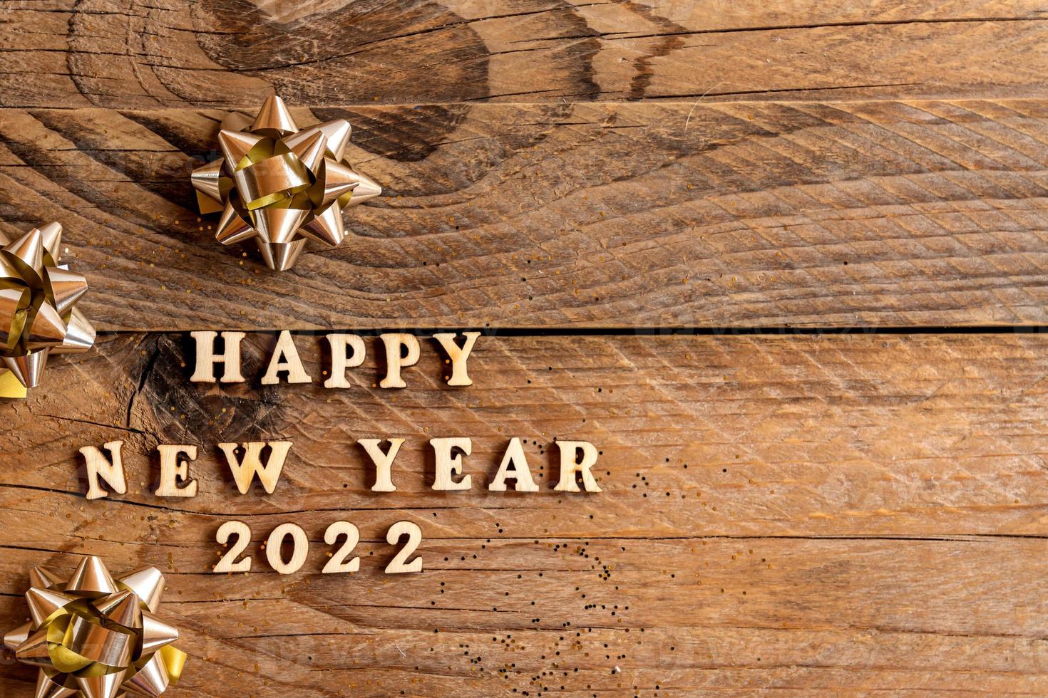 Happy new year 2022 inscription made with wooden letters decorated festive golden bows on wooden backgeound wih copy space. Greeting card for new year celebration photo