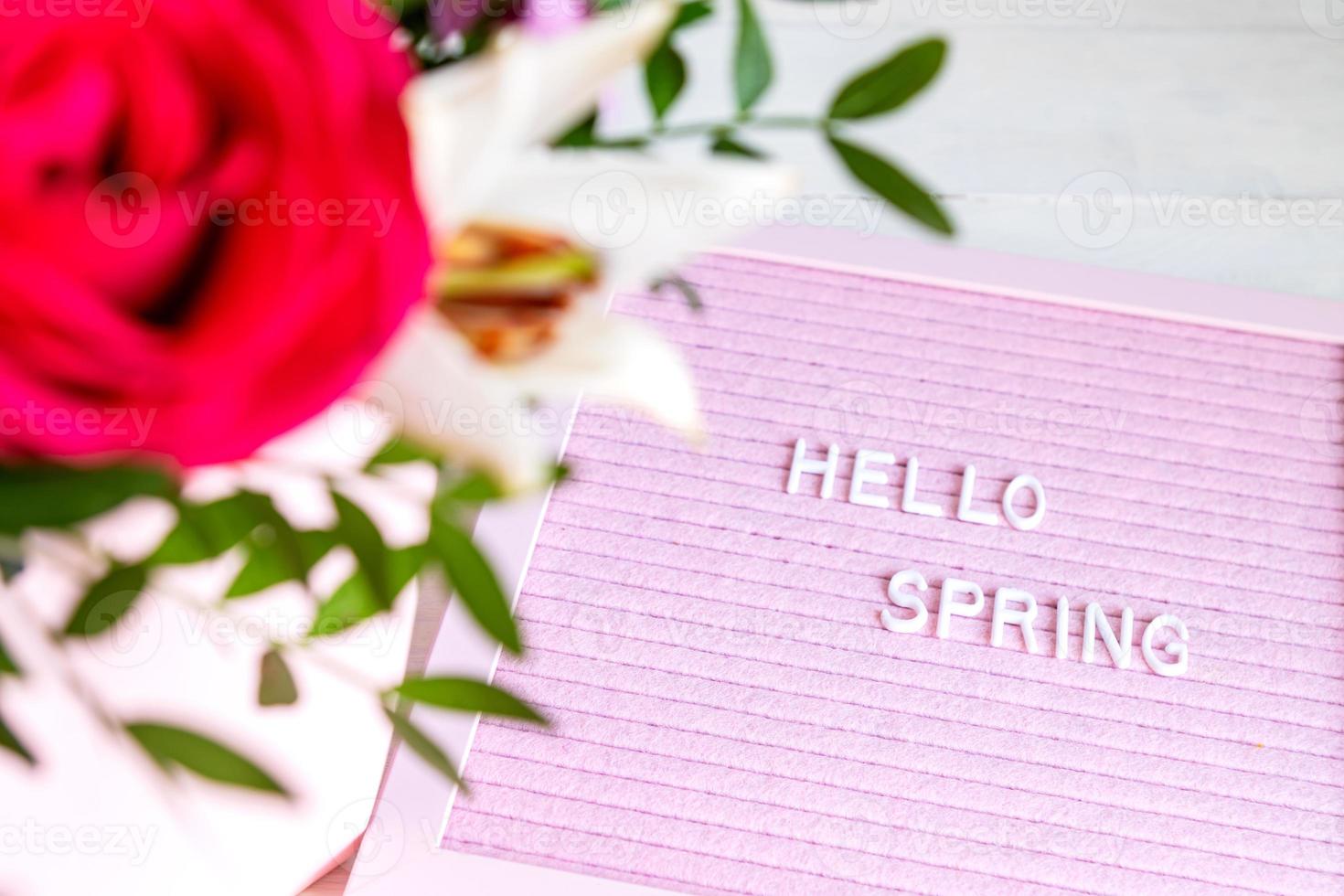 Text Hello Spring on pink letter board and bouquet of colored flowers. Concept Springtime mood and happiness. photo