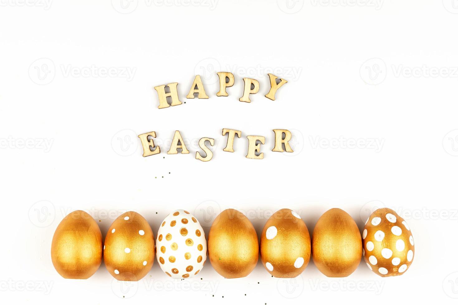 Easter festive decoration. Top view of easter eggs colored with golden paint and inscription in English Happy Easter. Wooden letters on white background. Various dotted design photo