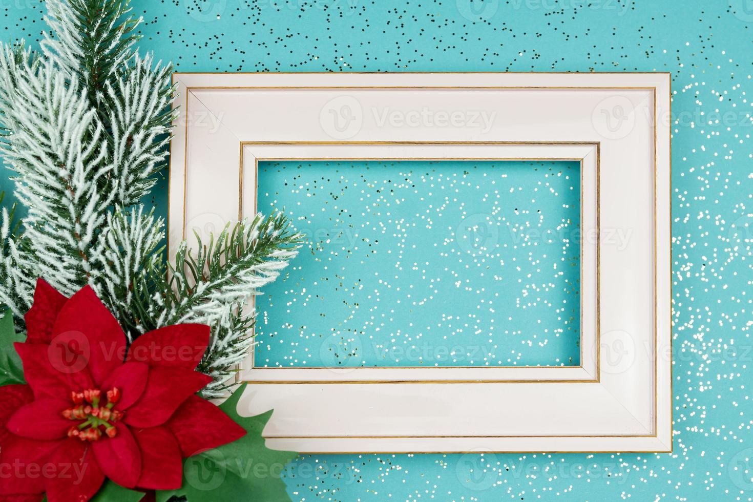 Festive greeting card for Christmas with photo frame, spruce tree branch and poinsettia on blue confetti background.