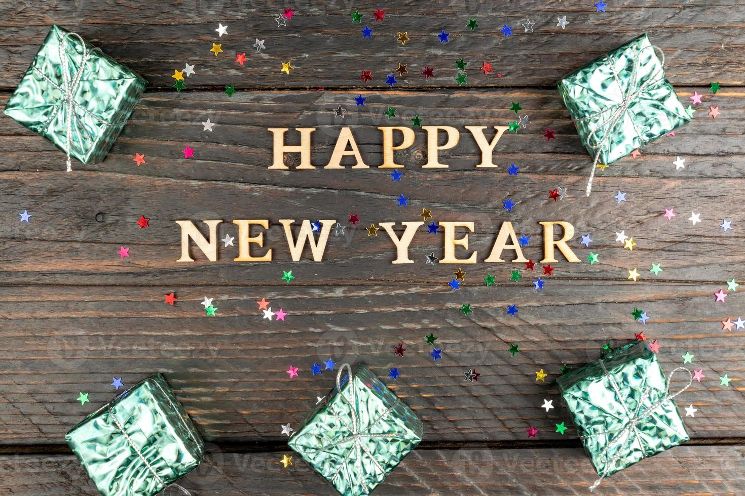 happy new year wooden text, scattered confetti and glitter gift boxes on a wooden background. Festive holiday concept photo