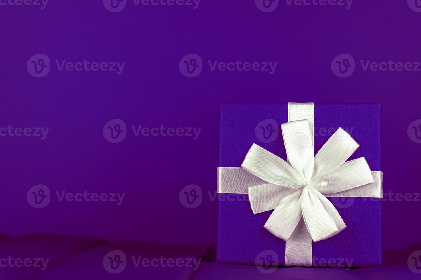 bonochrome violet celebration creeting card, gidt box with tied white bow on purple bckground with copy space. photo