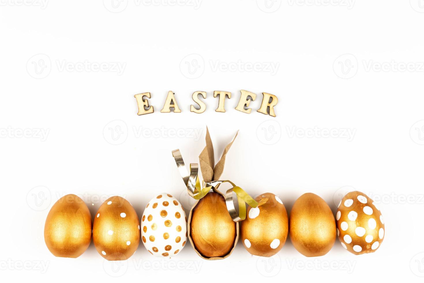 Easter festive decoration. Top view of easter eggs colored with golden paint and inscription in English Happy Easter. Wooden letters on white background. Various dotted design photo