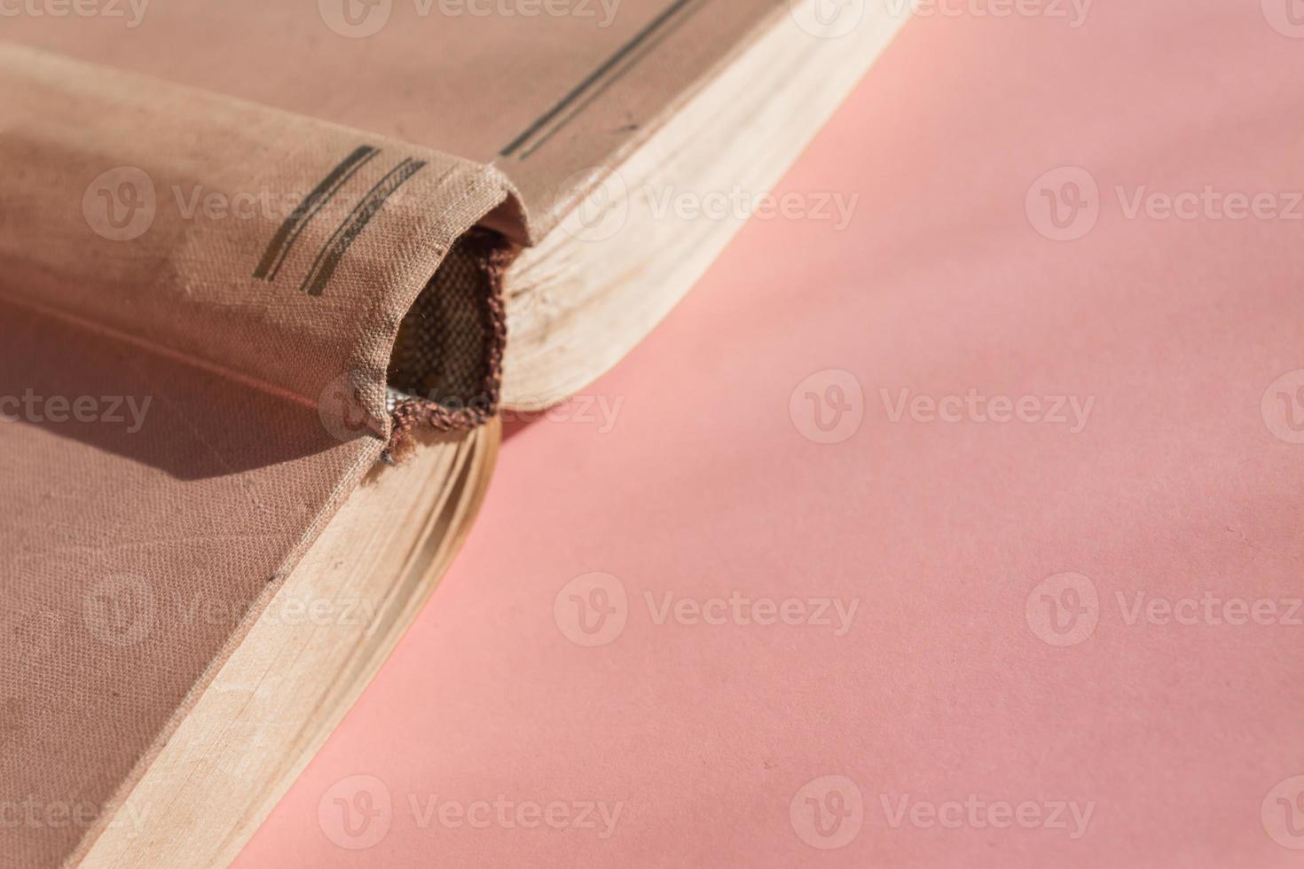 Open hardcover old book on pink background with copy space. Educational concept photo