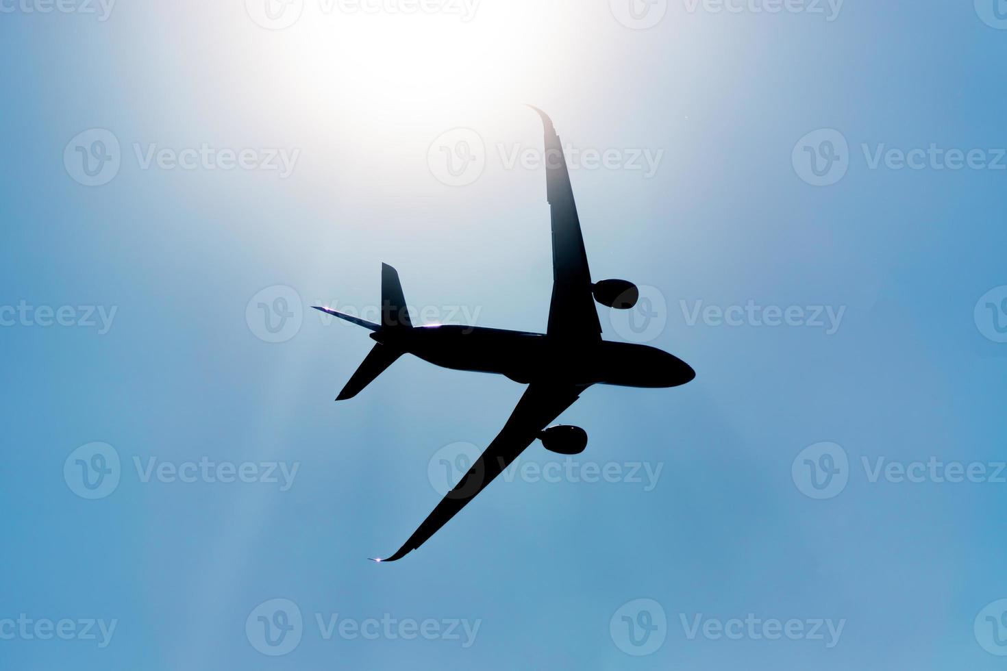 Silhouette of an airplane flying in the sky under the sun. photo