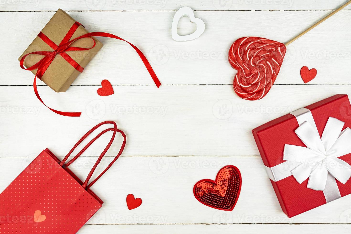 Creative Valentine Day romantic composition with red hearts, satin ribbon, lollipop, gift box and paper bag on white background. Mockup with copy space for blogs and social media. photo
