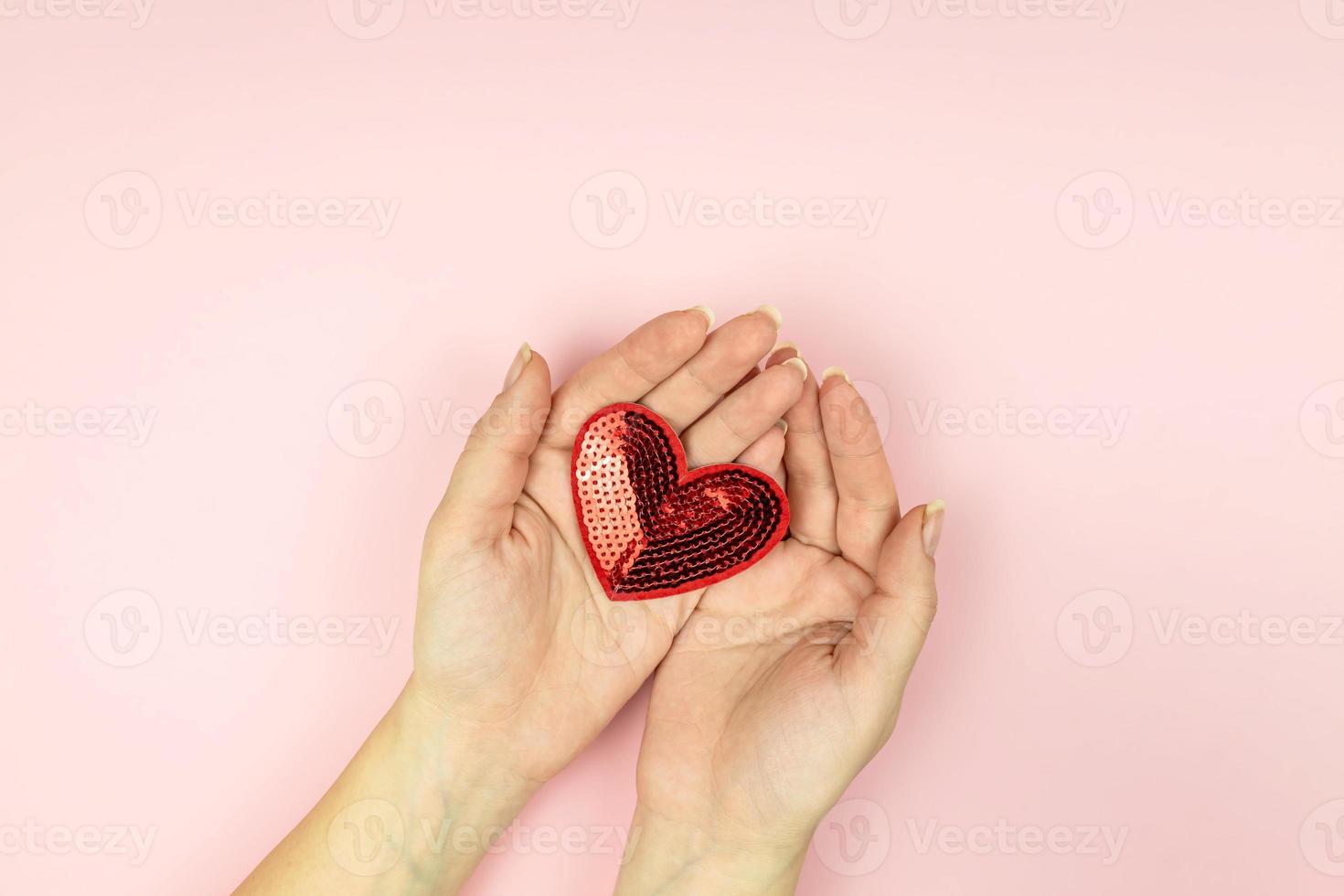 Female hands holding red sequin heart on pink background. Creative minimal layout with copy space photo