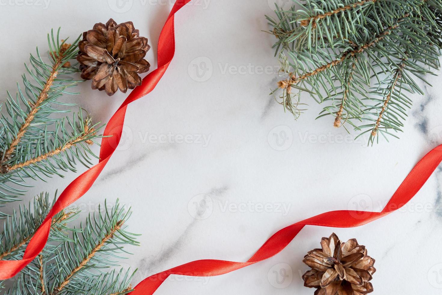 tarjeta de felicitación de navidad y año nuevo con espacio de copia. ramas de coníferas azules, conos y cinta de satén roja dispuestas sobre fondo de mármol blanco foto