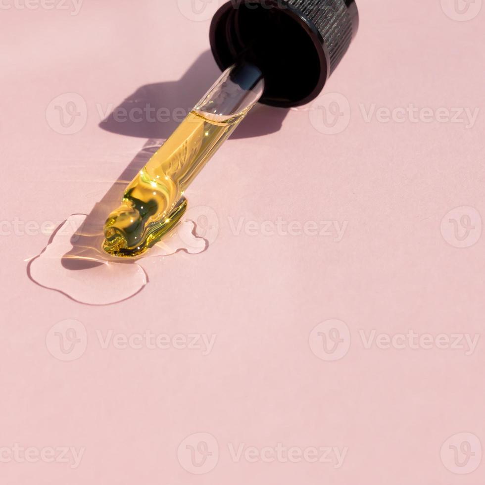 Bottle pipette dropper and Liquid yellow-orange retinol or vitamin c gel or serum on a pink background photo