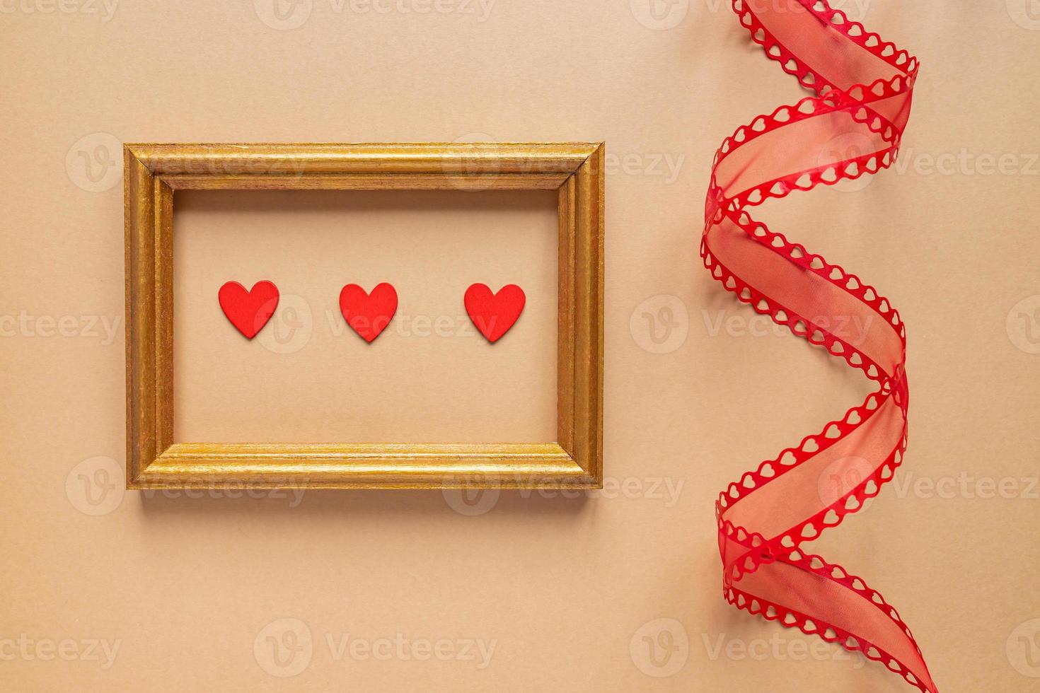 Valentine's day or Wedding romantic concept. Twisted decorative ribbon and golden photo frame with red hearts on beige background.