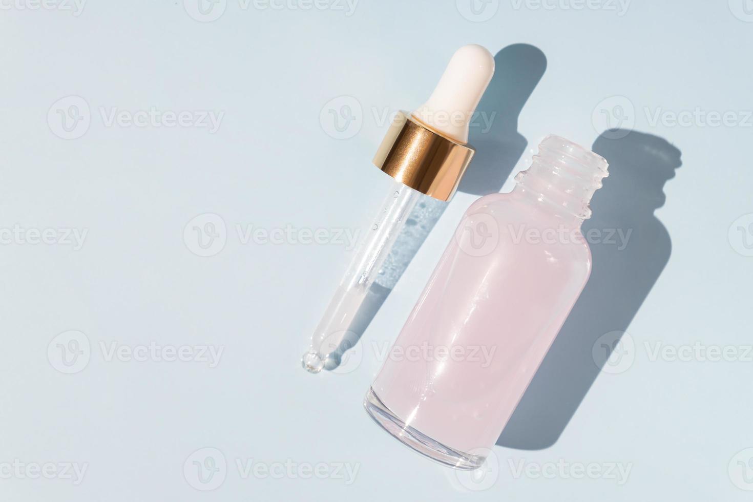 Top view of transparent dropper bottle with pink beauty face oil on blue background. anti aging serum with natural engredients. photo