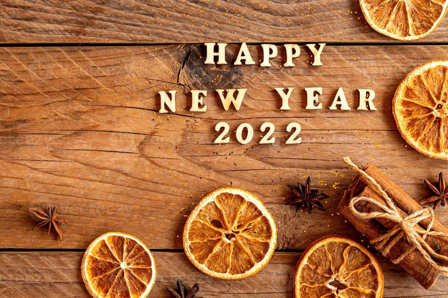 Cinnamon sticks, slices of dried orange, star anise and quote happy new year 2022 on wooden background with copy space. Top view. Christmas and New Year celebration concept. photo