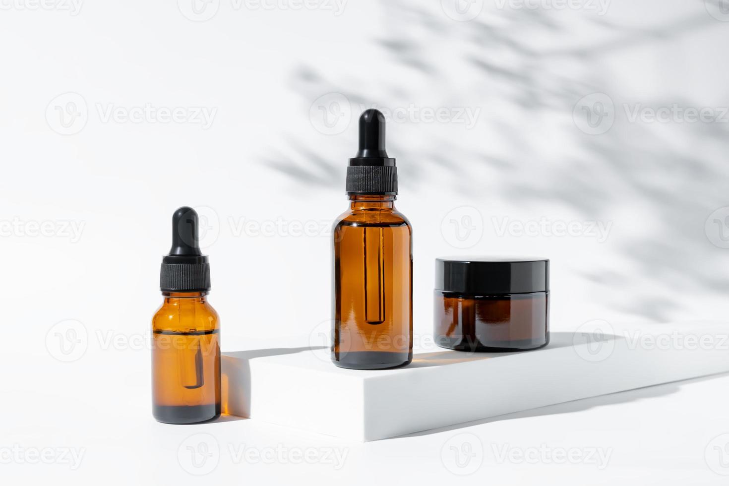 Natural cosmetics in amber glass packaging on white background with flowers shadows. SPA organic beauty products set. Skin care concept photo