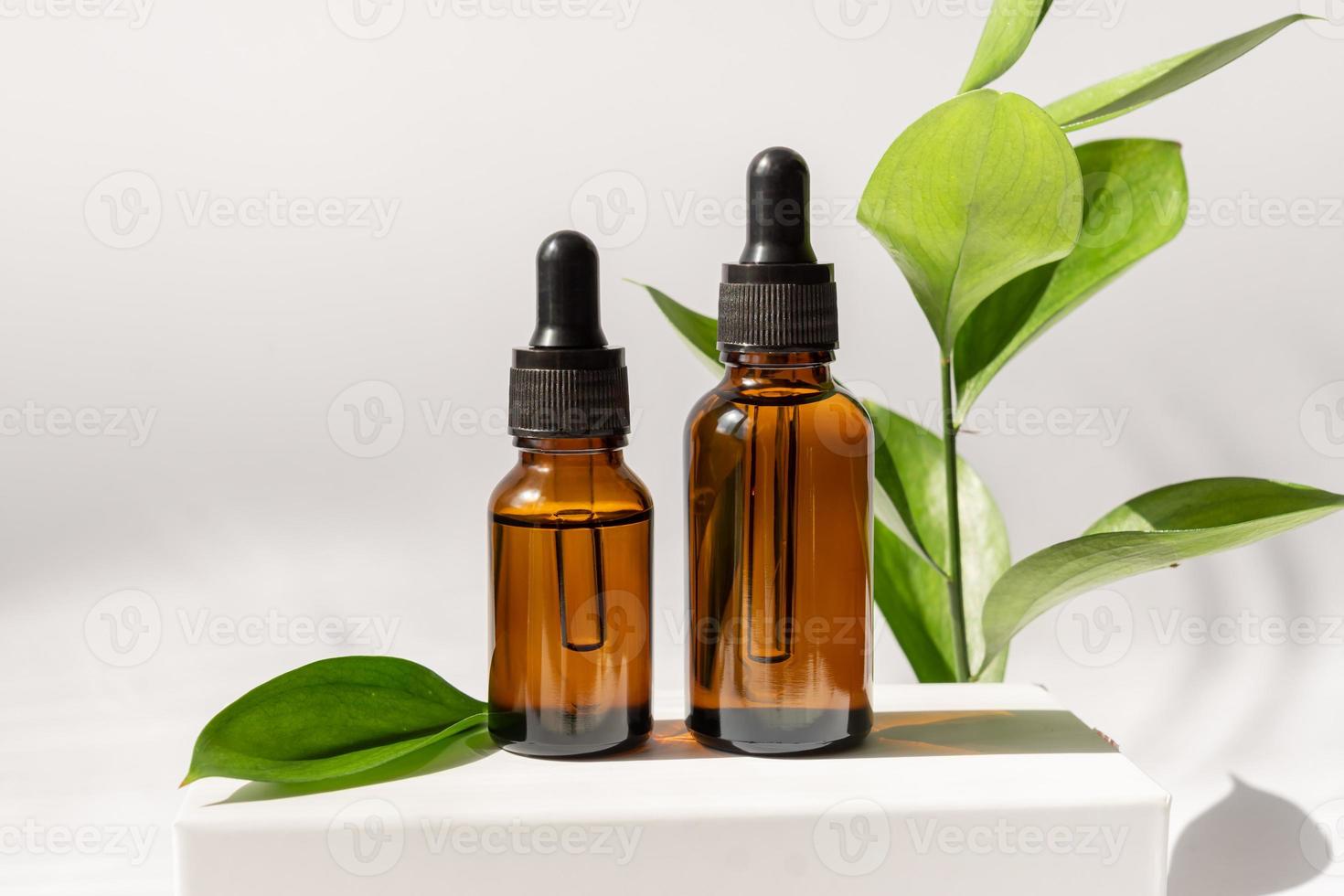 Amber cosmetic bottles with pipette on white podium, product packaging with natural ruscus branch, anti aging serum with peptides, cosmetics mockup, spa concept. photo