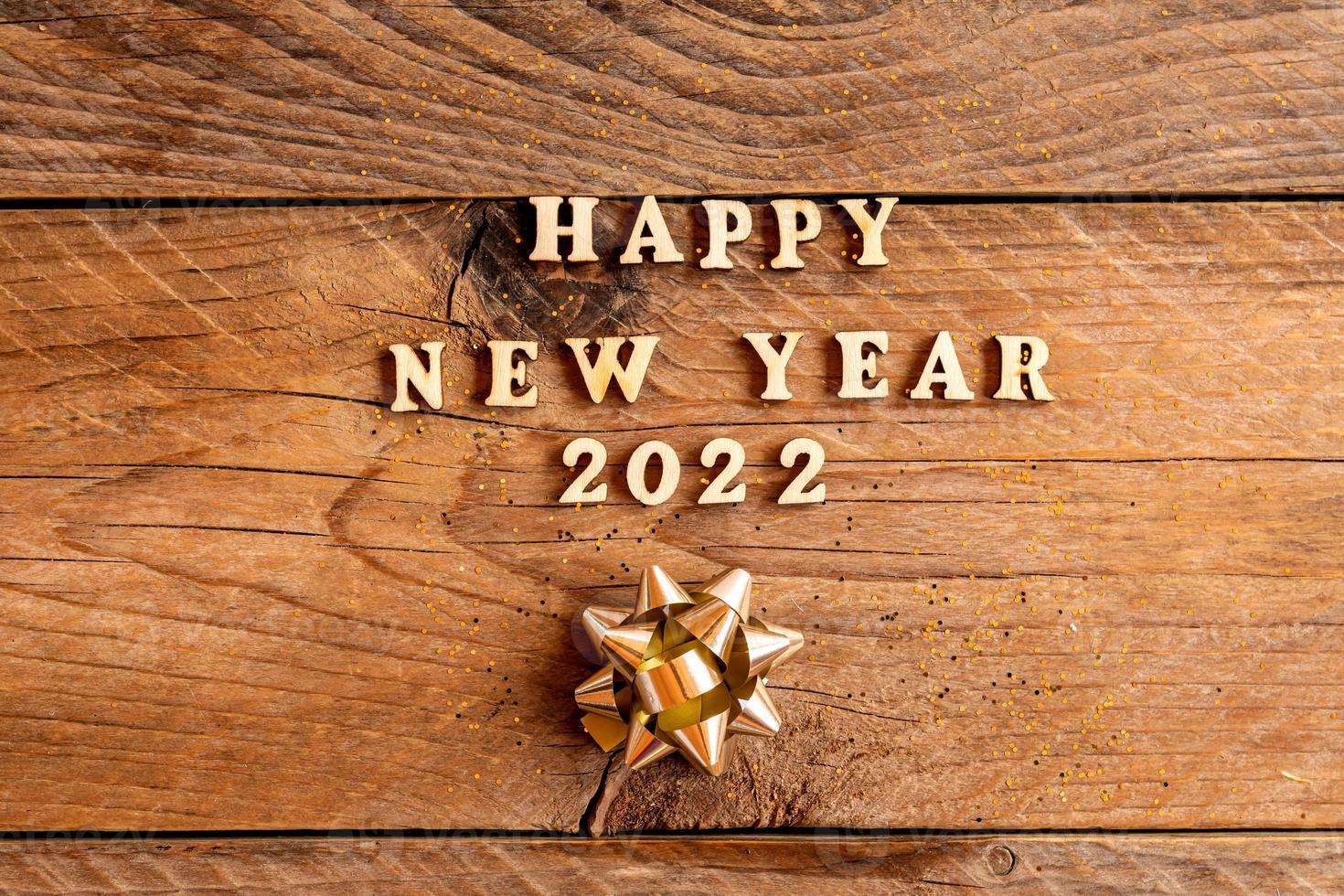 inscripción de feliz año nuevo 2022 hecha con letras de madera decoradas con arcos dorados festivos sobre fondo de madera con espacio de copia. tarjeta de felicitación para la celebración de año nuevo foto