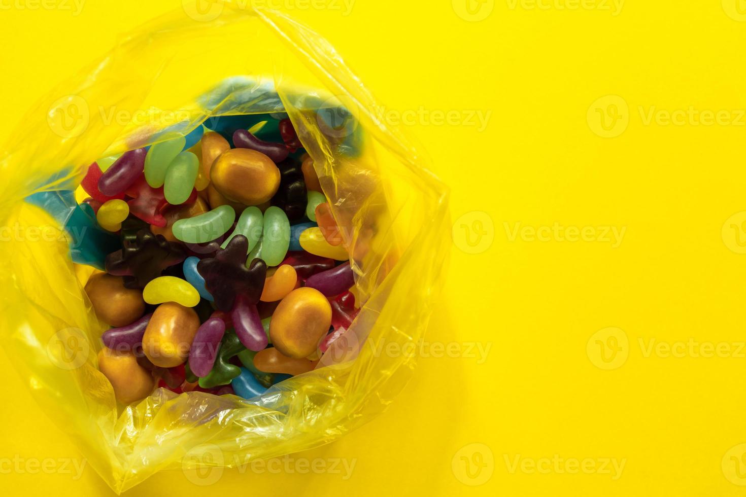 Multi-colored glazed jelly beans sweets in plastic package on yellow paper background photo