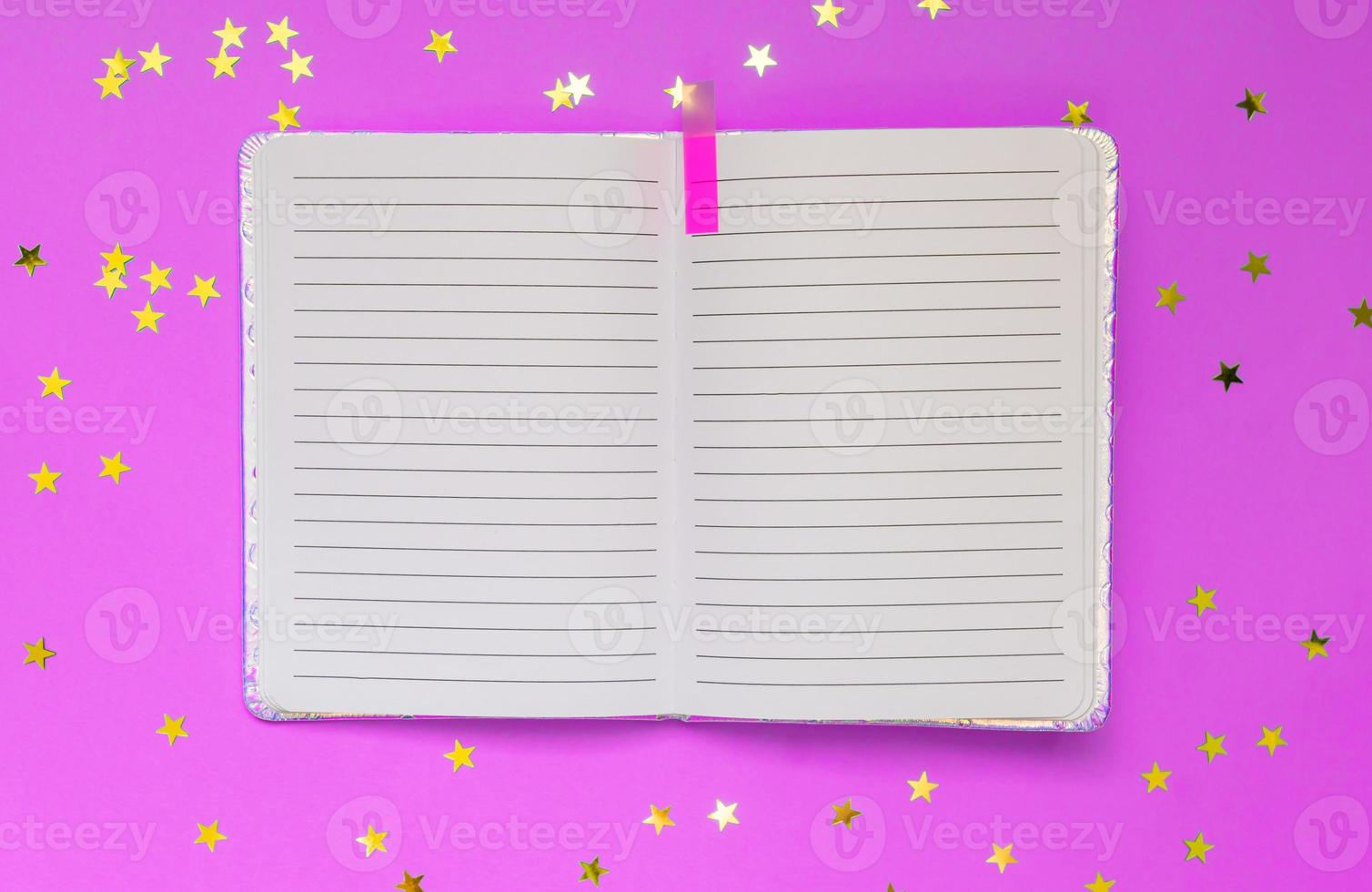 Open empty notebook on a pink background with stars confetti. Top view. Space for text or design photo