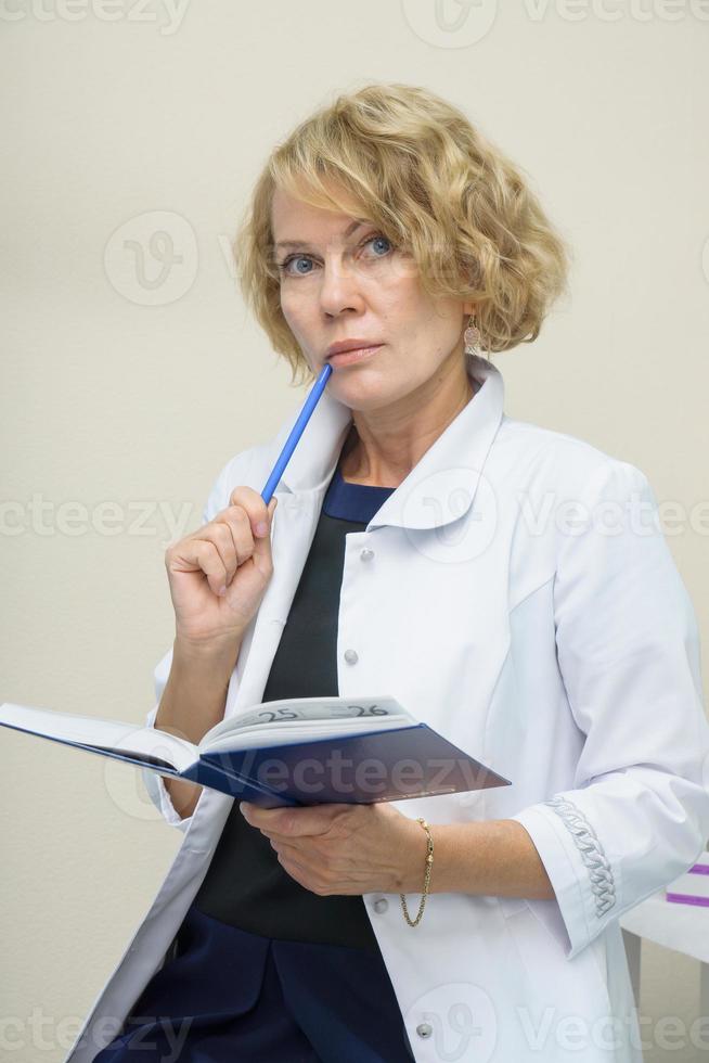 middle aged woman in white coat holding blue daily planner. Doctor female, medical professional photo