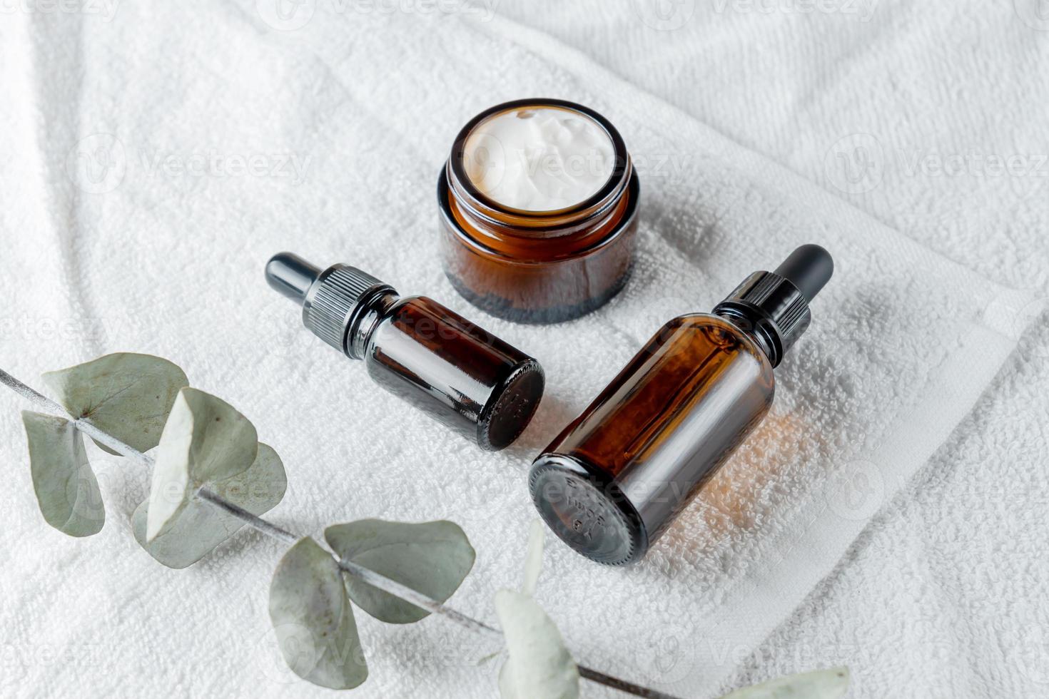 Brown glass bottles and eucalyptus branch on a white towel background. Eco-friendly organic natural cosmetics for skin and body care. Copy Space photo